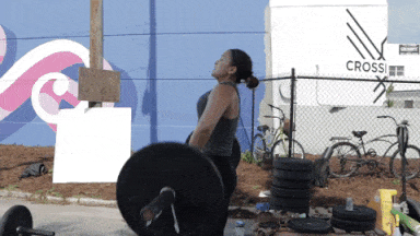 A woman lifts a very heavy barbell weight above her head in a lift outdoors at CrossFit727 - GIF