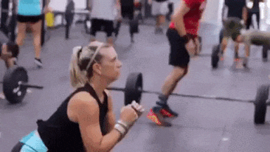 GIF of a blonde-haired woman doing squats in the foreground while other gym members work out in the background