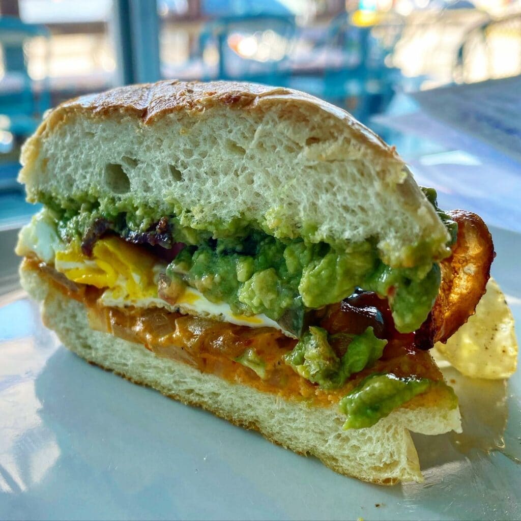 a stacked breakfast sandwich with avocado, eggs, and bacon