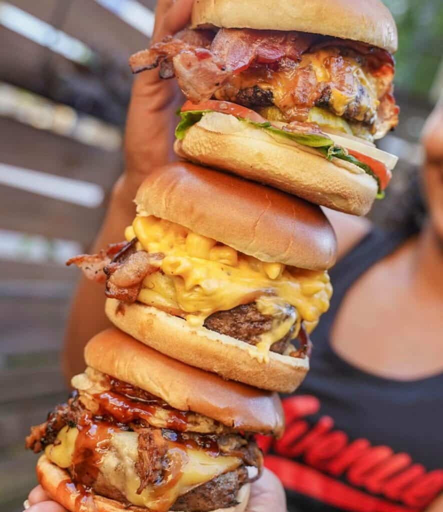 a stack of three cheeseburgers loaded with bacon, tomatoes, and lettuce.