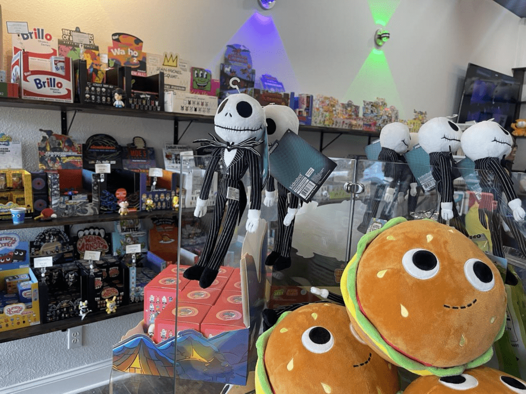 stuffed animals in the shape of hamburgers and skeletons displayed in front of toy shelves.